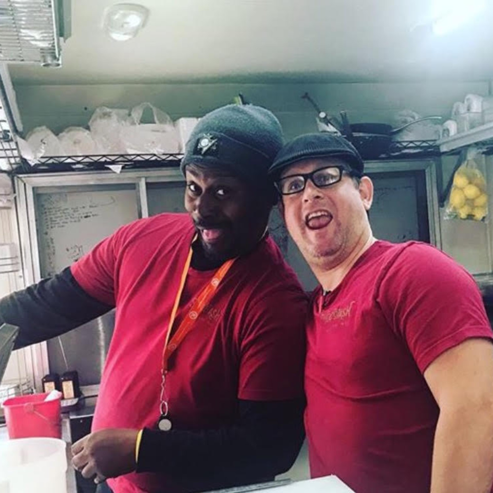 Two male Succotash kitchen staff in red shirts and hats smiling playfully at the camera.