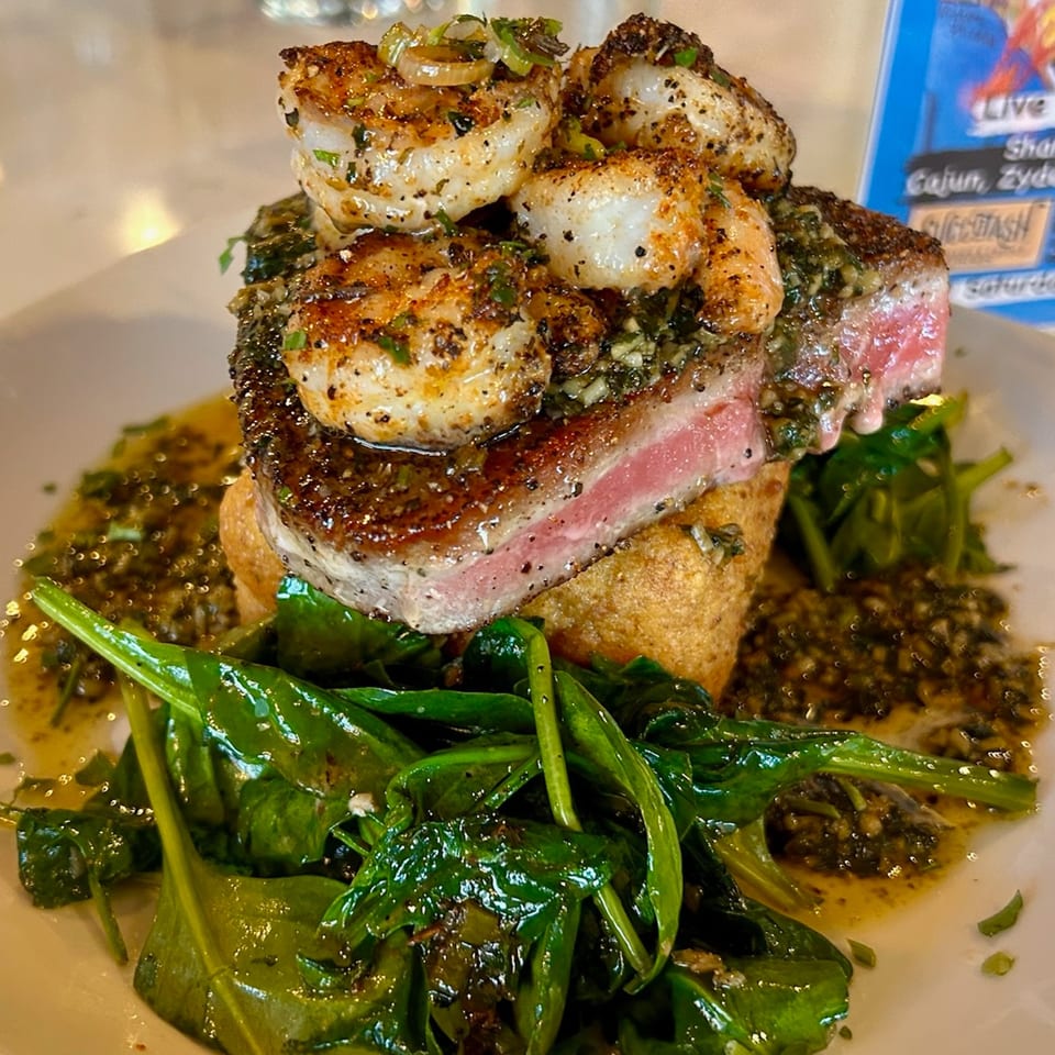 Seared tuna steak topped with seasoned shrimp, served over greens and a savory sauce.