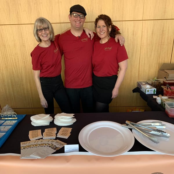 Three smiling Succotash staff in red shirts stand behind a table with plates and brochures.