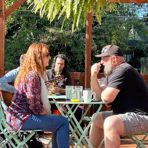 Patrons enjoying live music on the sunny outdoor patio at Succotash Southern and Creole Kitchen.